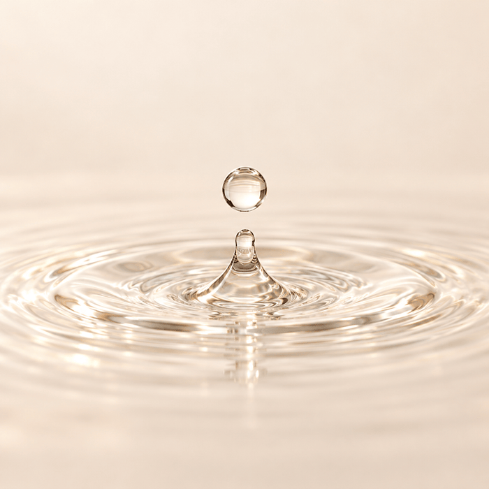Clear water droplet splashing into a shallow pool, representing moisture care.